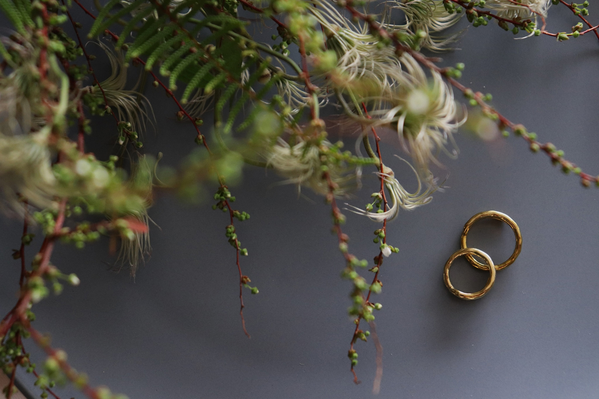 ゴールドの結婚指輪が2つ、グリーンの枝と一緒にテーブルに置かれている